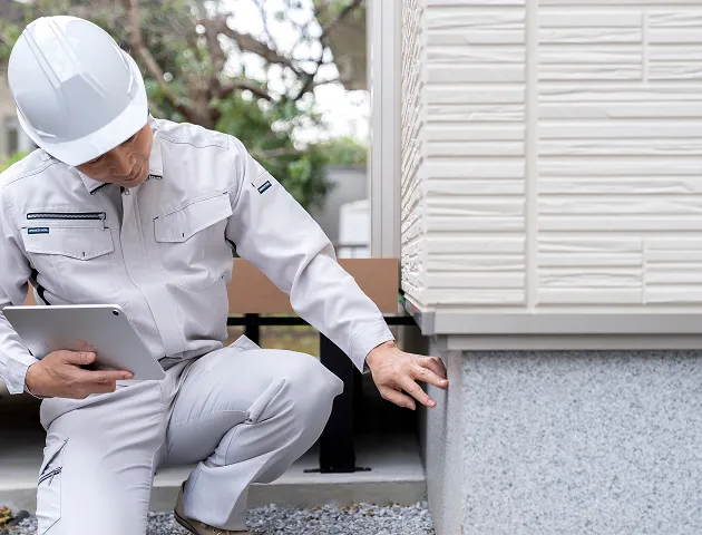 ヘルメットをかぶり作業着を着た建設作業員が改修中の建物内で工具を持っている様子